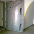 3-atü-Tür aus dem Bunker in den Notausgang Richtung Norden. Da in der Vergangenheit immer wieder ungebetene Gäste vorbeischauten, hat die Feuerwehr diesen Zugang zusätzlich gesichert (Stahlprofil im oberen Teil zur Verriegelung). Rechts ist wieder ein drei Meter langer Tunnelstutzen zu sehen, der eine eindringende Druckwelle entschärfen sollte und deren zerstörerische Kraft an das massive Gestein ableiten sollte.