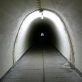 Blick in den präzise 159 Meter und 25 Zentimeter langen Stollen hinter dem Tunnelknick des Notausgangs. Unter den Bodenplatten waren Kabel verlegt, während von oben auch der Postbunker mit eindringendem Bergwasser zu kämpfen hatte, das in die Drainage ablief. Am Ende ist die für eine Bunkeranlage vergleichsweise leichte Gittertür zu sehen.